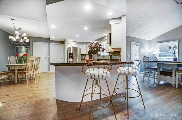 kitchen featuring stainless steel fridge, a breakfast bar area, white cabinets, kitchen peninsula, and light wood-type flooring