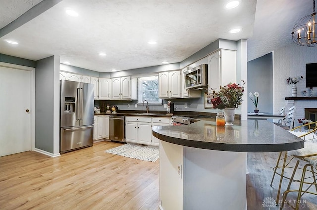 kitchen featuring appliances with stainless steel finishes, white cabinets, a kitchen bar, kitchen peninsula, and light wood-type flooring