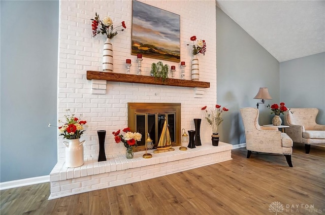 living area with vaulted ceiling, a brick fireplace, and hardwood / wood-style floors