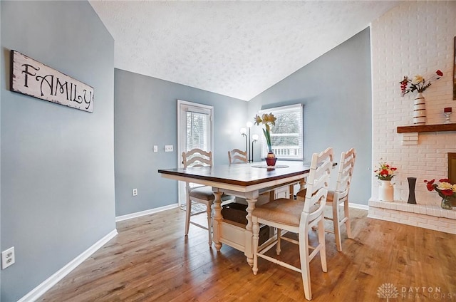 dining space with lofted ceiling, a textured ceiling, light hardwood / wood-style floors, and a brick fireplace