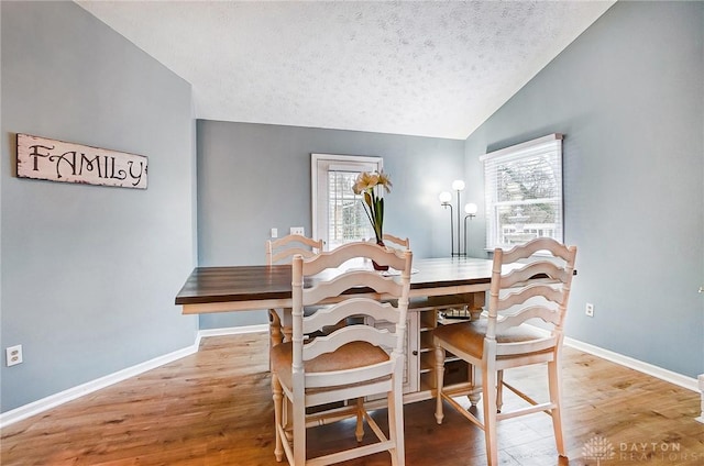 dining room featuring hardwood / wood-style flooring, vaulted ceiling, and a textured ceiling