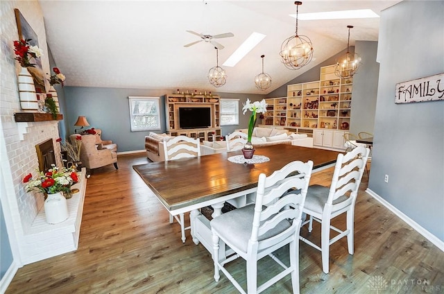 dining room with hardwood / wood-style flooring, vaulted ceiling, ceiling fan with notable chandelier, and a fireplace