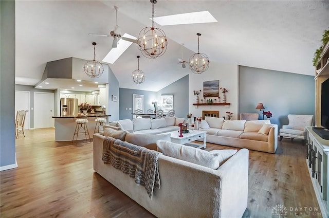 living room with ceiling fan with notable chandelier, high vaulted ceiling, a skylight, and hardwood / wood-style floors