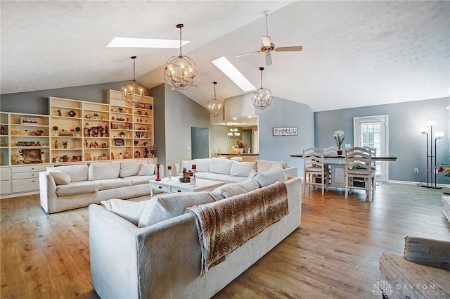 living room with ceiling fan with notable chandelier, high vaulted ceiling, a skylight, light wood-type flooring, and a textured ceiling