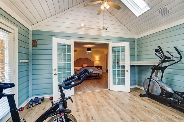 workout room with lofted ceiling with skylight, ceiling fan, light hardwood / wood-style floors, and french doors