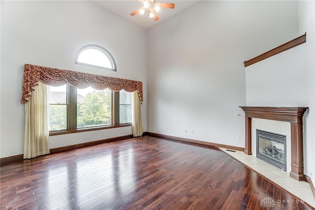 unfurnished living room featuring ceiling fan, high vaulted ceiling, light wood-type flooring, baseboards, and a tile fireplace