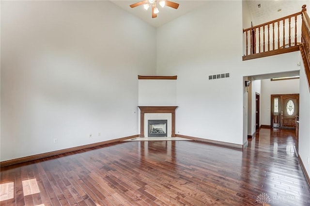 unfurnished living room featuring visible vents, baseboards, dark wood-style floors, a fireplace with flush hearth, and ceiling fan