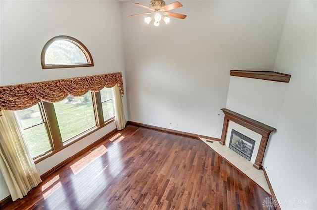 unfurnished living room featuring a high ceiling, a fireplace, wood finished floors, a ceiling fan, and baseboards