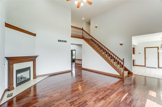 unfurnished living room with visible vents, stairway, a fireplace with flush hearth, wood finished floors, and baseboards