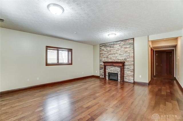 unfurnished living room featuring a textured ceiling, baseboards, wood finished floors, and a stone fireplace