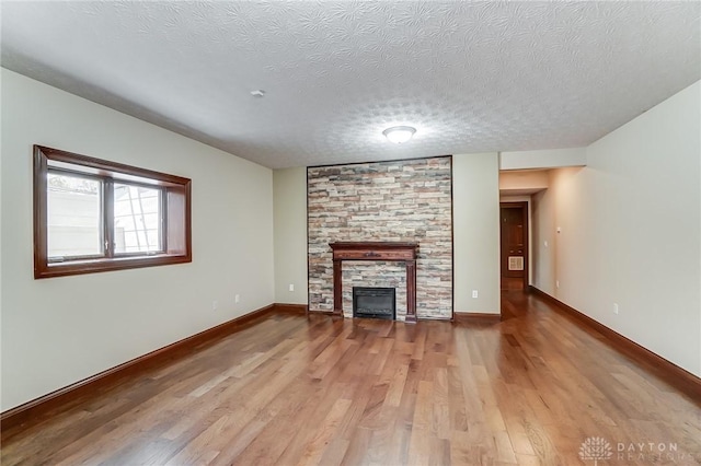 unfurnished living room with a textured ceiling, a stone fireplace, light wood-type flooring, and baseboards