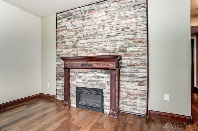 unfurnished living room with a textured ceiling, baseboards, wood finished floors, and a glass covered fireplace