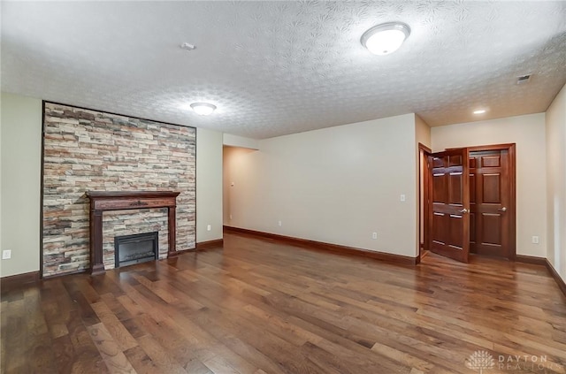 unfurnished living room with a textured ceiling, a stone fireplace, dark wood-type flooring, and baseboards