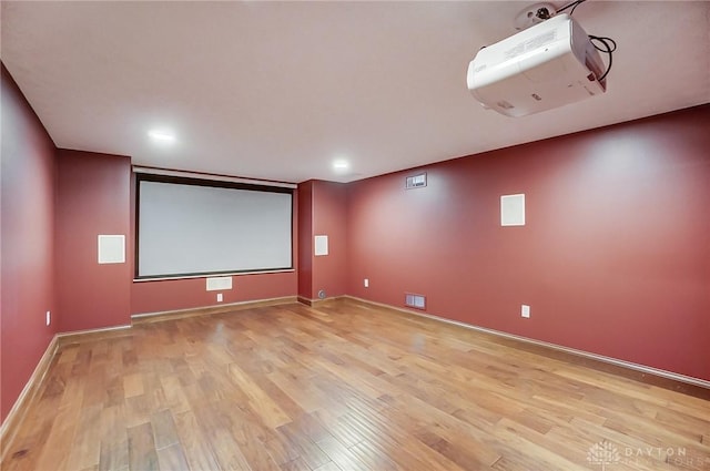 cinema room with visible vents, light wood-style flooring, and baseboards