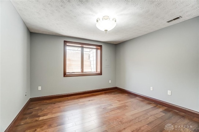 empty room with a textured ceiling, wood finished floors, visible vents, and baseboards