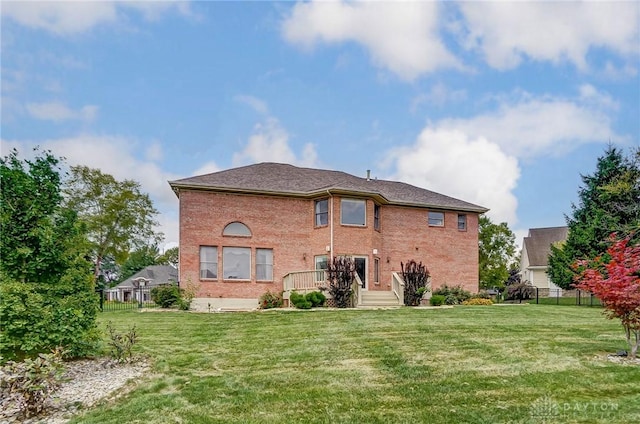 back of property with brick siding, a lawn, and fence