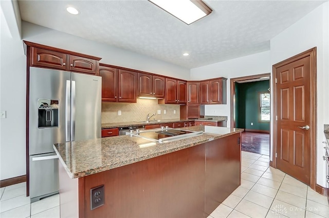 kitchen with light tile patterned floors, appliances with stainless steel finishes, a kitchen island with sink, a sink, and light stone countertops