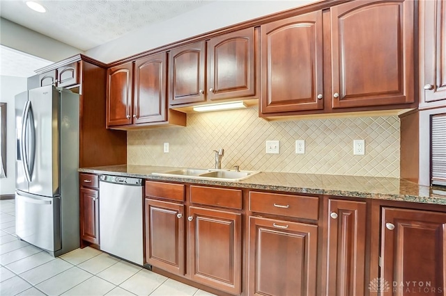 kitchen with stainless steel appliances, decorative backsplash, light tile patterned flooring, a sink, and light stone countertops