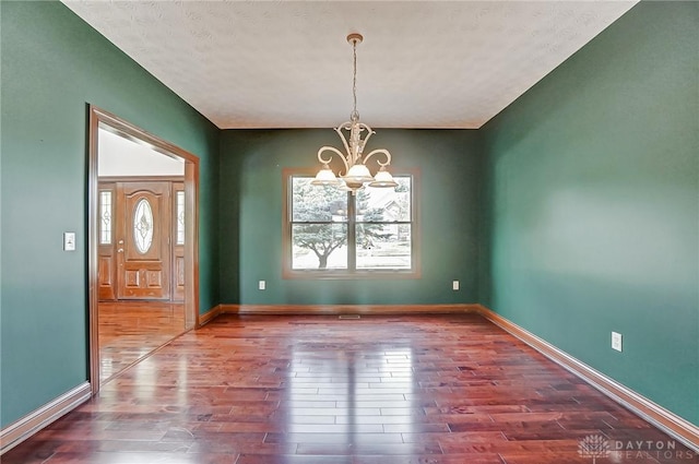 unfurnished dining area with a notable chandelier, baseboards, and wood finished floors