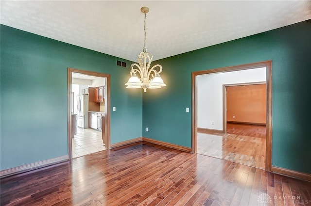 unfurnished room featuring a chandelier, visible vents, baseboards, and wood finished floors