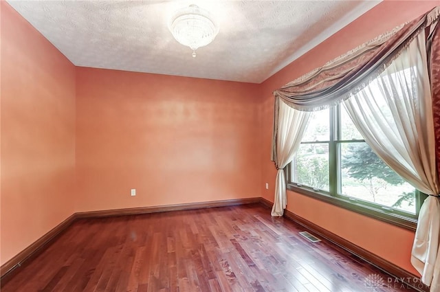 spare room with a textured ceiling, wood finished floors, visible vents, and baseboards