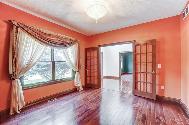 spare room featuring visible vents, a textured ceiling, baseboards, and wood finished floors