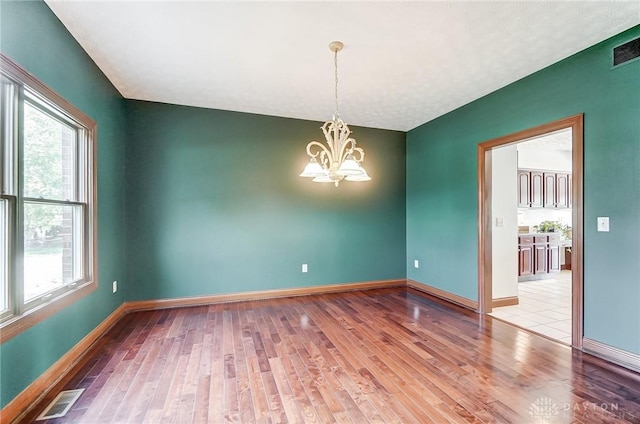 empty room with a notable chandelier, baseboards, and wood finished floors