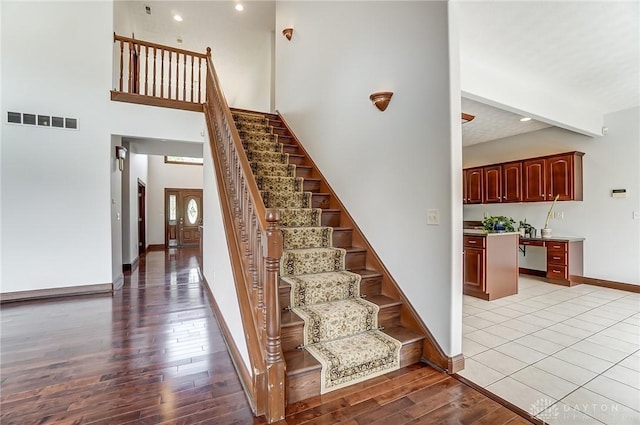 stairs featuring recessed lighting, a high ceiling, wood finished floors, visible vents, and baseboards