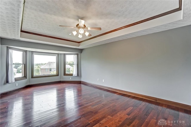 empty room featuring ornamental molding, a tray ceiling, dark wood-style flooring, and a textured ceiling