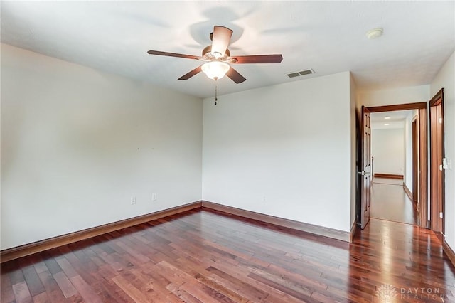 spare room with a ceiling fan, visible vents, baseboards, and wood finished floors