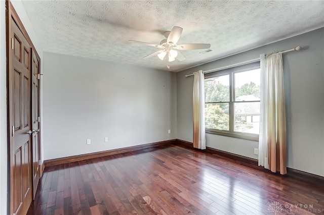 spare room featuring ceiling fan, dark wood-style flooring, a textured ceiling, and baseboards