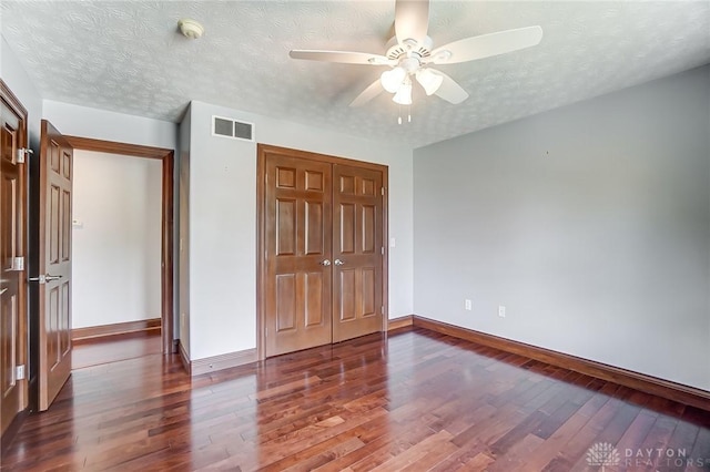 unfurnished bedroom with a textured ceiling, dark wood-type flooring, visible vents, and baseboards