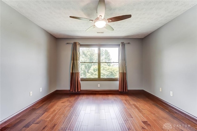 spare room featuring visible vents, ceiling fan, a textured ceiling, wood finished floors, and baseboards