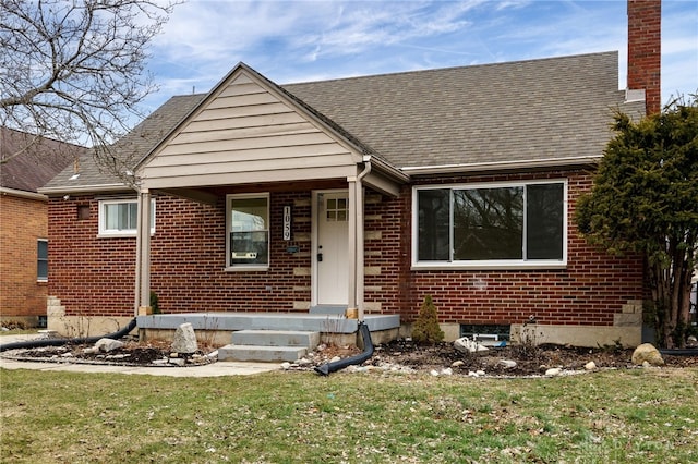 bungalow-style house with a front yard, brick siding, and a chimney