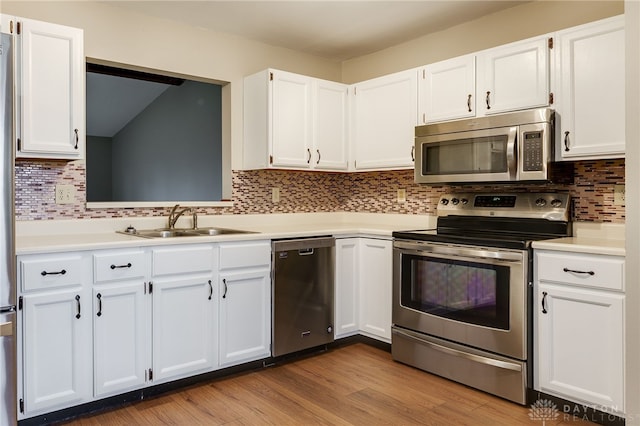 kitchen featuring appliances with stainless steel finishes, tasteful backsplash, white cabinetry, sink, and light hardwood / wood-style floors