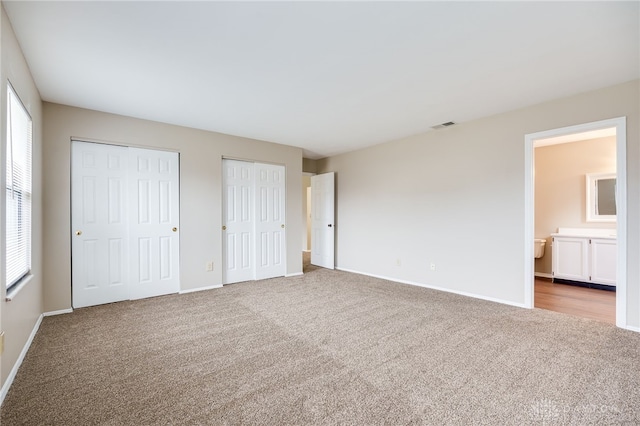 unfurnished bedroom with light carpet, two closets, and multiple windows