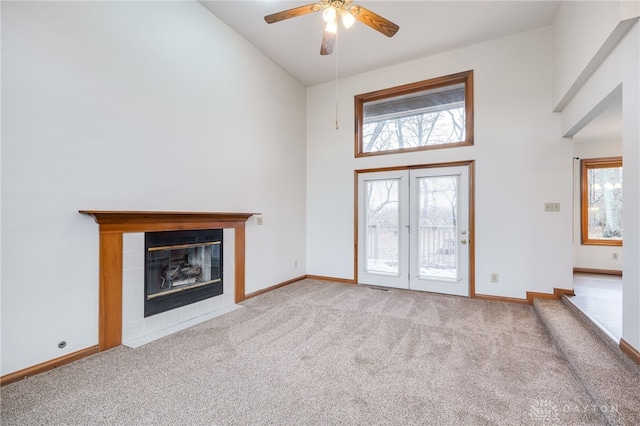 unfurnished living room featuring a tiled fireplace, high vaulted ceiling, light colored carpet, and ceiling fan