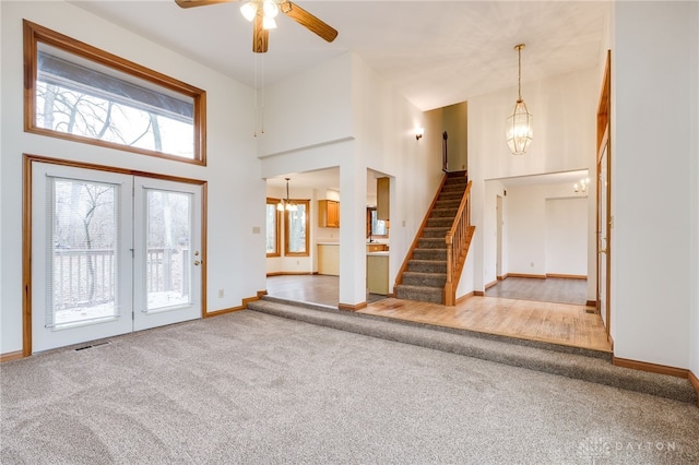 carpeted entryway featuring plenty of natural light, ceiling fan with notable chandelier, and a high ceiling