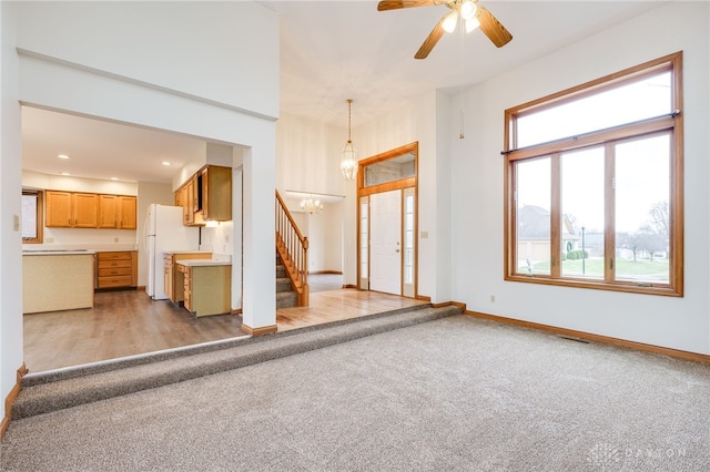 unfurnished living room featuring ceiling fan with notable chandelier and light colored carpet