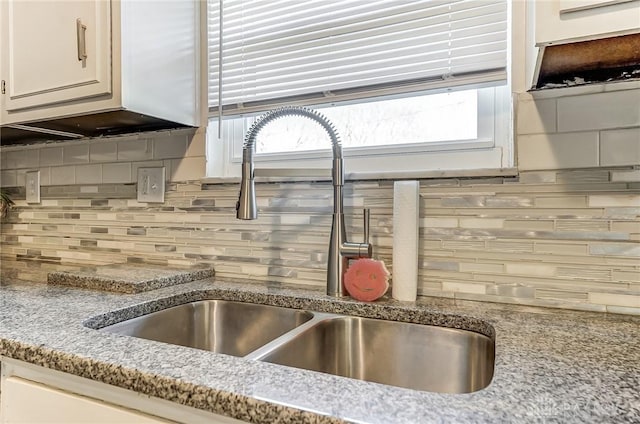 interior details with sink, backsplash, light stone countertops, and white cabinets