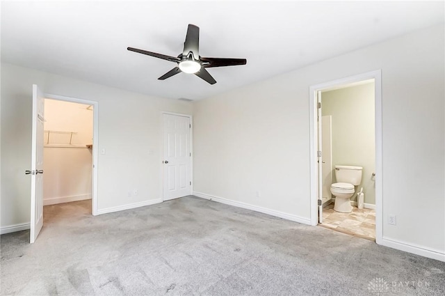 unfurnished bedroom featuring a walk in closet, light colored carpet, ceiling fan, ensuite bath, and a closet