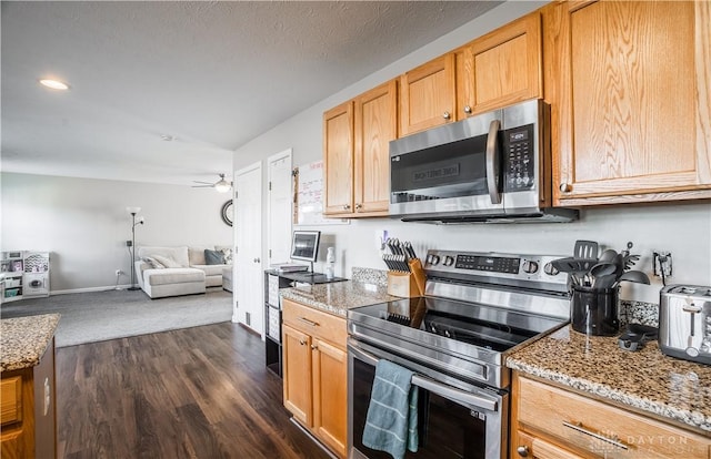 kitchen featuring ceiling fan, light stone counters, stainless steel appliances, dark wood-type flooring, and a textured ceiling