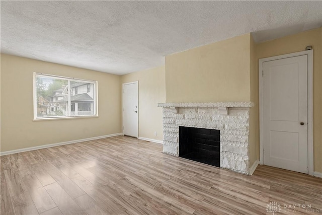 unfurnished living room with a stone fireplace, a textured ceiling, and light hardwood / wood-style flooring