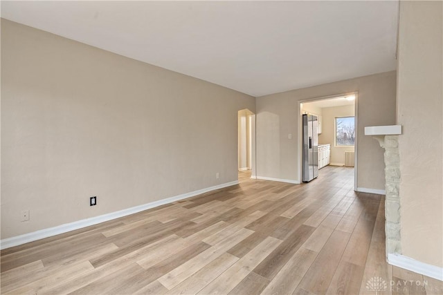 empty room with radiator heating unit and light hardwood / wood-style flooring