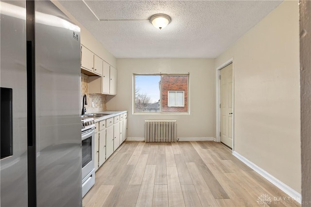 kitchen featuring sink, white cabinetry, light wood-type flooring, appliances with stainless steel finishes, and radiator heating unit