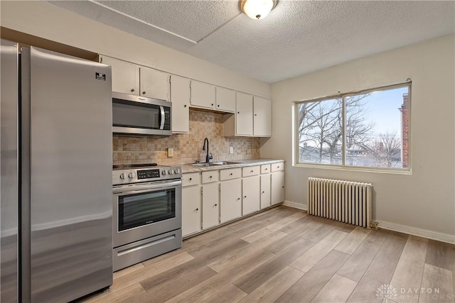 kitchen featuring light hardwood / wood-style flooring, appliances with stainless steel finishes, white cabinetry, backsplash, and radiator heating unit