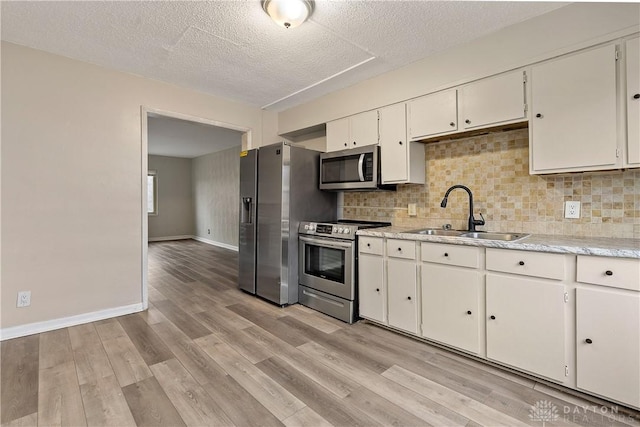 kitchen featuring sink, appliances with stainless steel finishes, white cabinetry, light hardwood / wood-style floors, and decorative backsplash