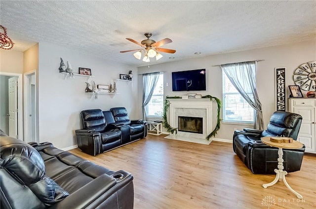 living room with a premium fireplace, ceiling fan, a textured ceiling, and light wood-type flooring