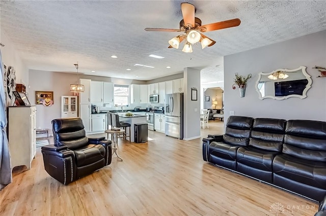 living room featuring ceiling fan, sink, a textured ceiling, and light wood-type flooring