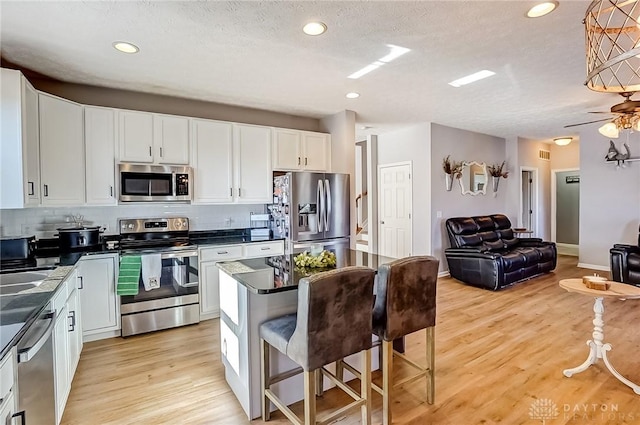 kitchen with white cabinetry, a center island, light hardwood / wood-style flooring, a kitchen breakfast bar, and stainless steel appliances